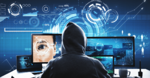 A person in a hoodie is sitting in front of multiple computer screens displaying biometric data, graphs, and security-related information, symbolizing cyber surveillance, cybersecurity threats, or data hacking.